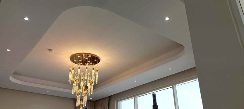 Layered gypsum ceiling with recessed lights above a double-height room