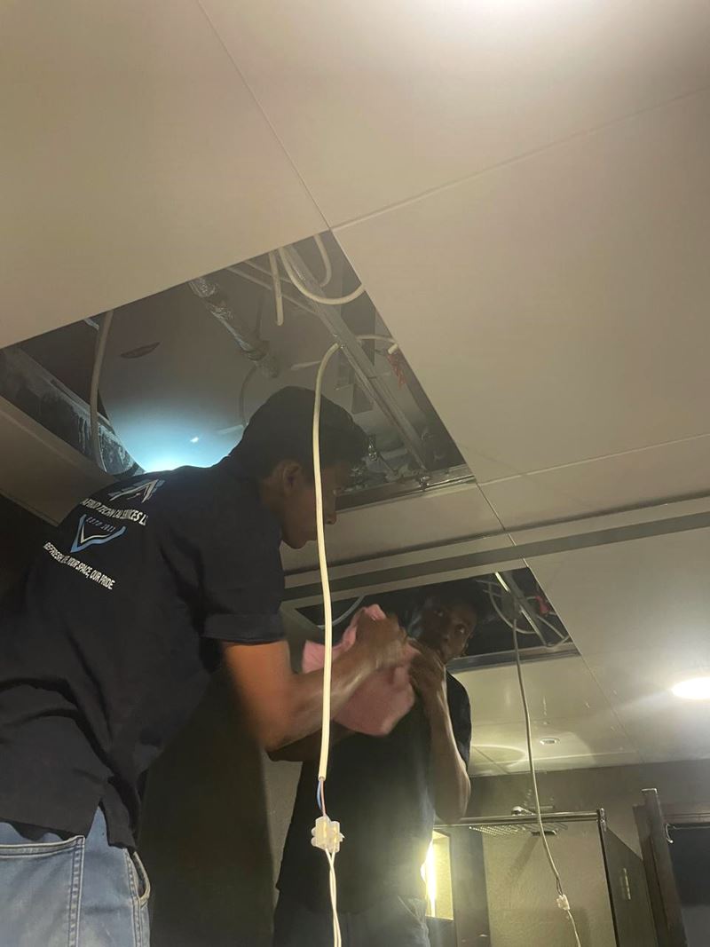 Technician inspecting services above an open bathroom ceiling during a maintenance visit