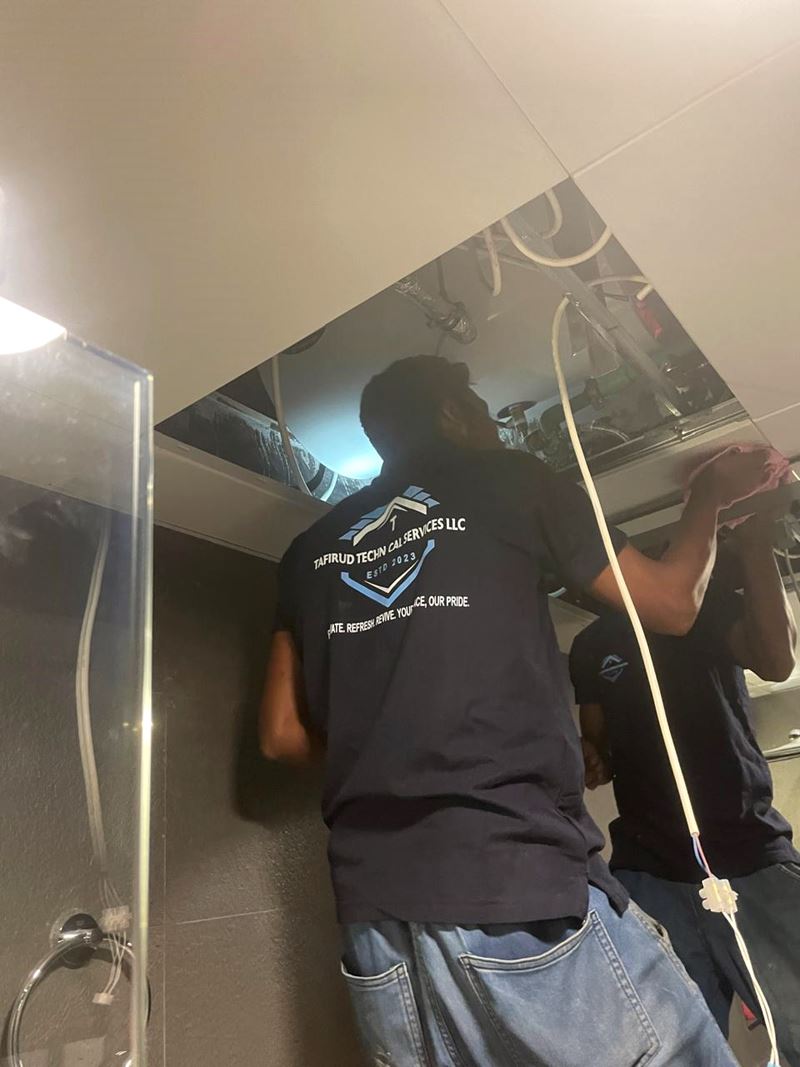 Tafirud technician in branded uniform routing cables through an open ceiling
